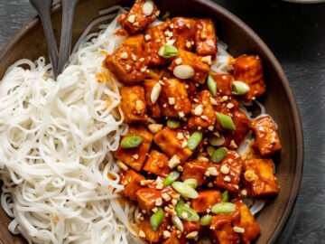 bowl filled with baked tofu in a spicy peanut sauce with peanuts and scallions on top