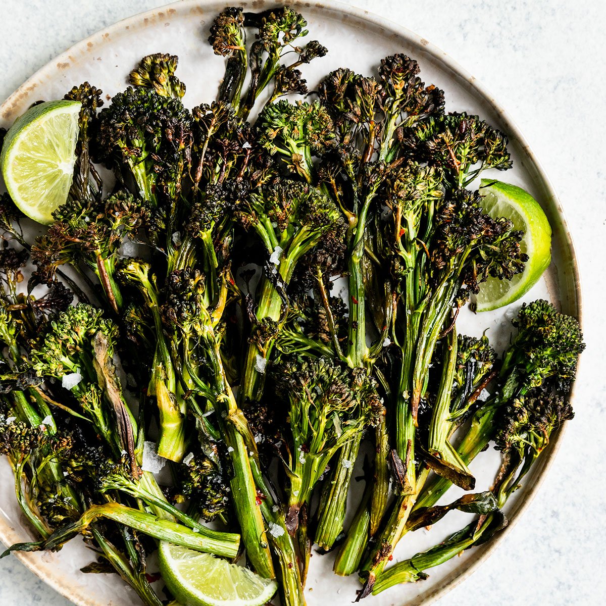 a plate full of broccolini with lime wedge and flaky salt