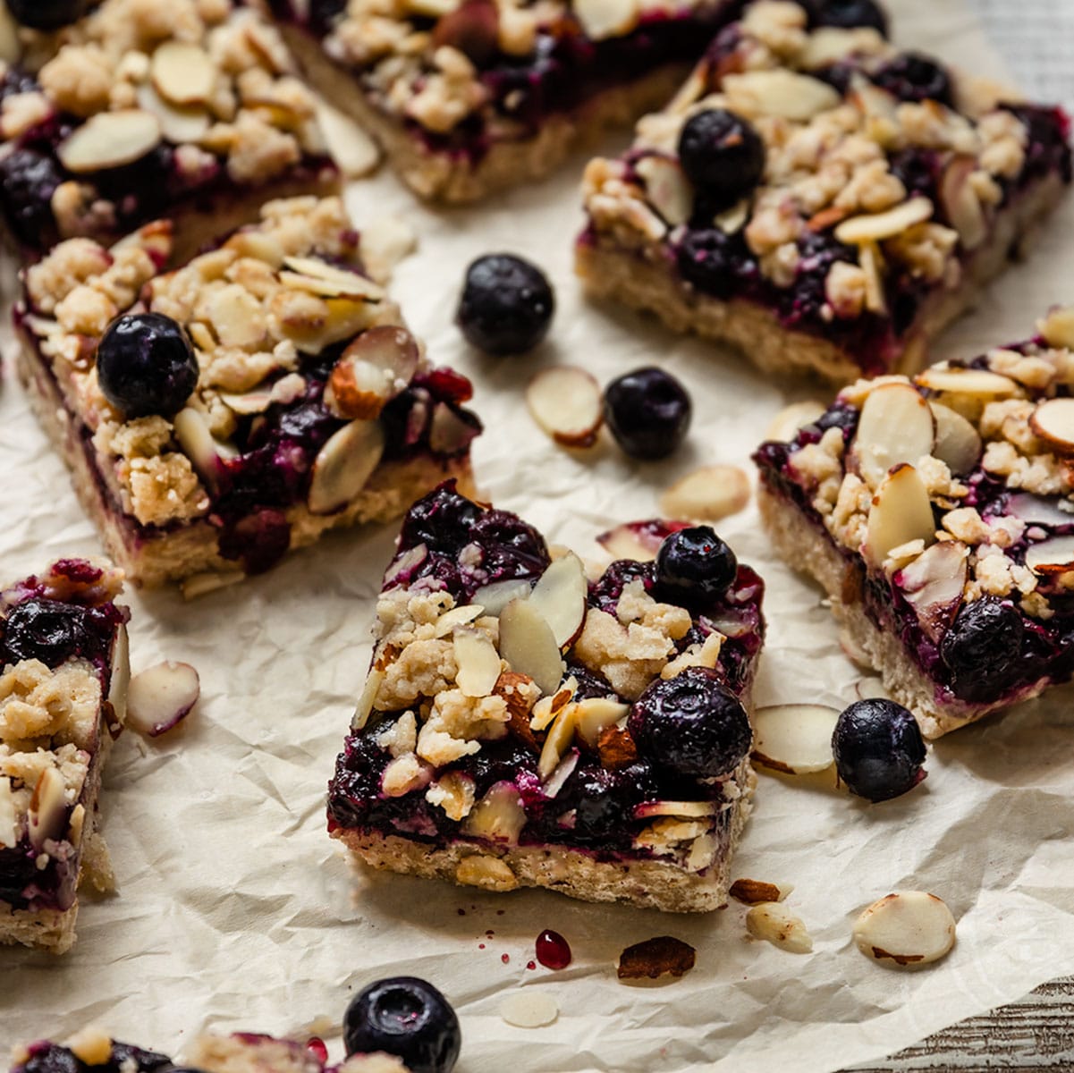 blueberry layer bars with almond crumble and blueberries on top of parchment paper