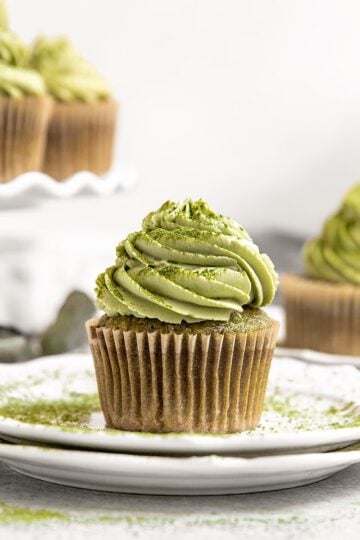 plate with a matcha green cupcake on top with matcha frosting and a dusting of matcha powder around and on top of the cupcake