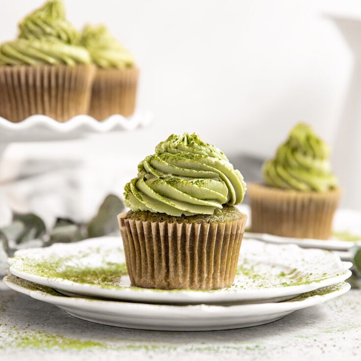 plate with a matcha green cupcake on top with matcha frosting and a dusting of matcha powder around and on top of the cupcake