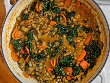 a large pot full of a brown stew with lentils, carrots, mushrooms, and kale