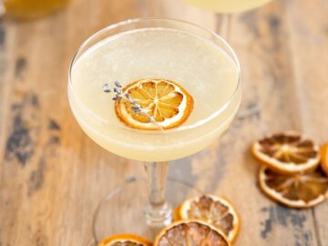 a martini cocktail glass filled with a lemon drop with a dried lemon slice and dried lavender spring as garnish