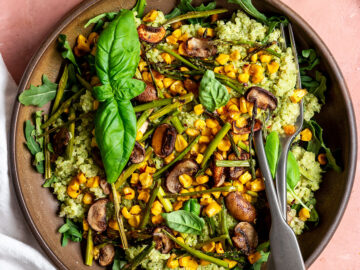 bowl filled with quinoa, pesto, corn, arugula, mushrooms, asparagus, and basil