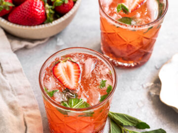two mojitos with strawberrise and mint alongside a bowl of strawberries