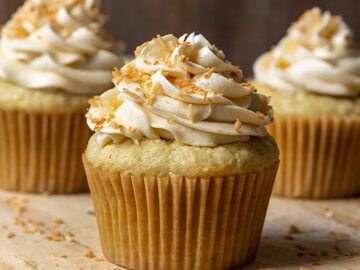a close up shot of three coconut cupcakes with frosting and toasted coconut on top