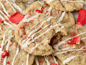 pile of strawberry cookies with vanilla glaze and dried strawberries with top cookie missing a bite