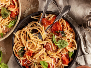 overhead shot of three bowls of pasta with cherry tomatoes, basil, and vegan parmesan
