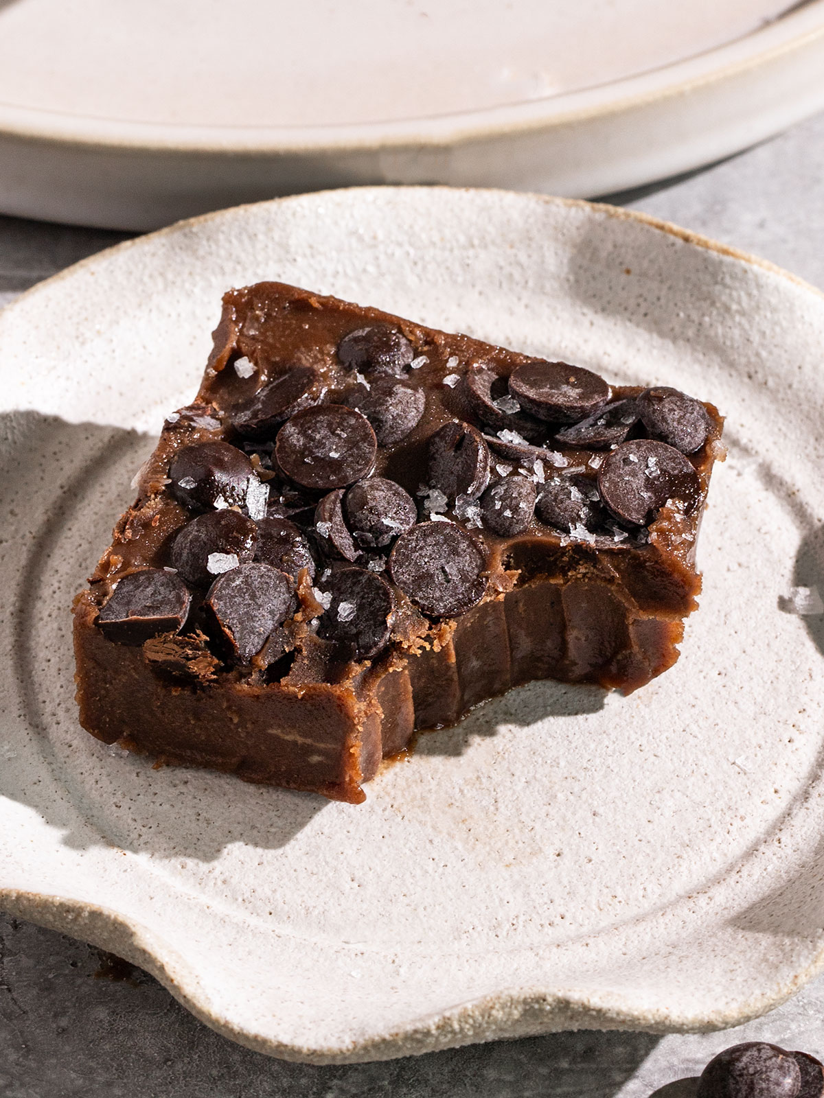 chocolate fudge with bite taken out and chocolate chips and salt on top of a plate.