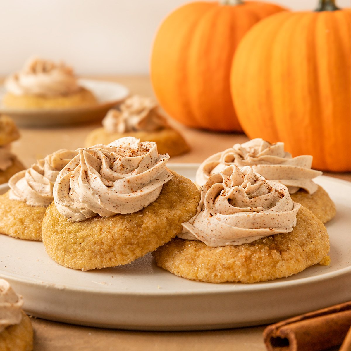 two frosted pumpkin sugar cookies on plate with pumpkins behind them