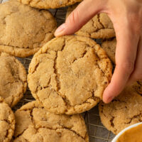 hand picking up peanut butter cookie from tray of cooking