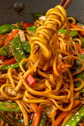 chopsticks that are pulling udon noodles and vegetables from a wok