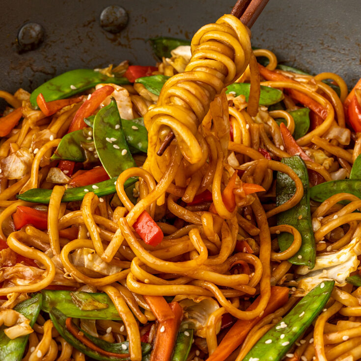 chopsticks that are pulling udon noodles and vegetables from a wok