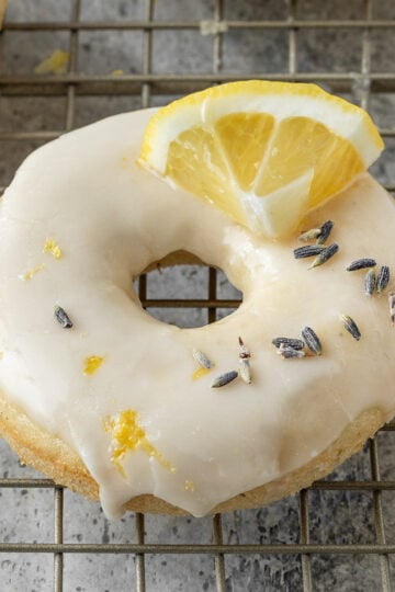 baked donut on wire rack with dried lavender, lemon glaze, lemon zest, and a fresh lemon slice on top