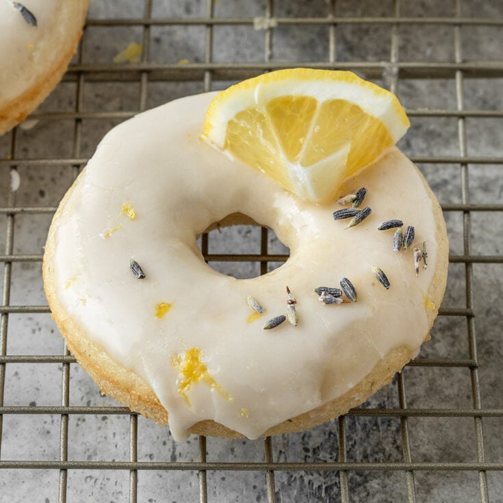 baked donut on wire rack with dried lavender, lemon glaze, lemon zest, and a fresh lemon slice on top