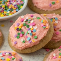 sugar cookies topped with pink frosting and rainbow sprinkles.