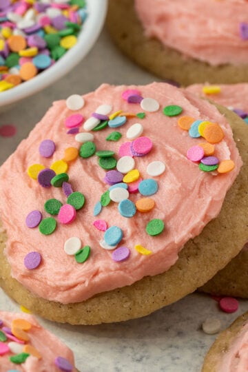 sugar cookies topped with pink frosting and rainbow sprinkles.
