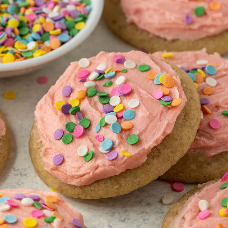 sugar cookies topped with pink frosting and rainbow sprinkles.