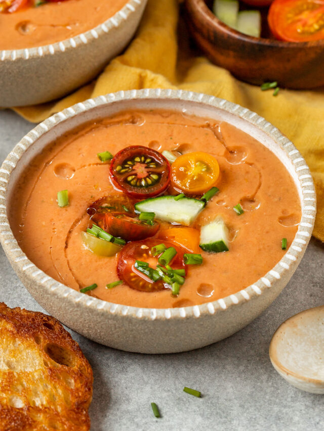 bowl of tomato gazpacho topped with tomatoes chives cucumber and oil drizzle.