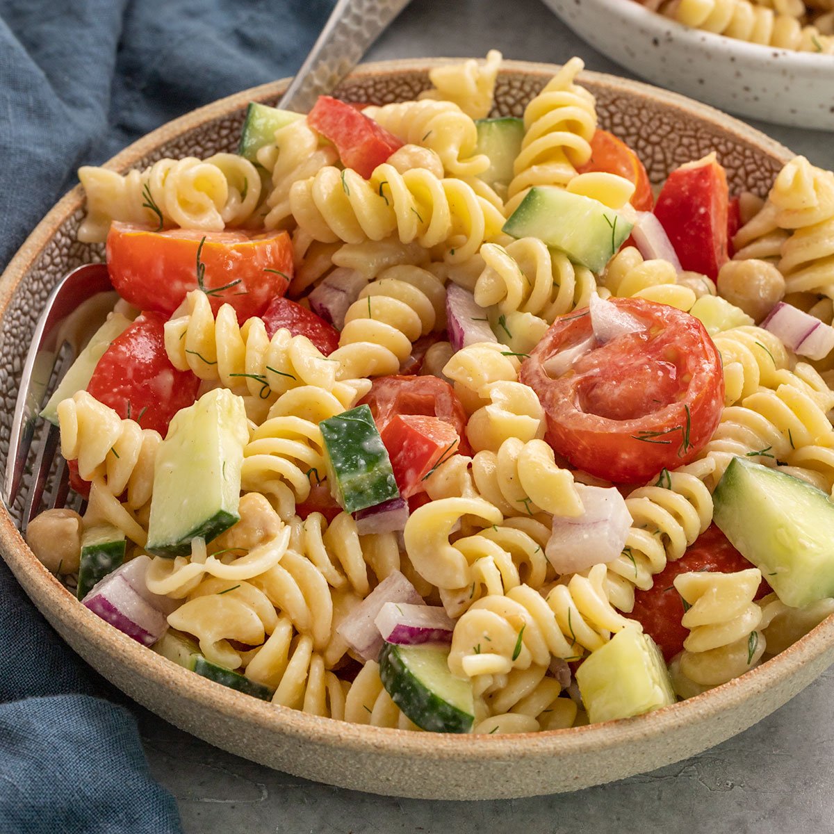 bowl of pasta salad with tomatoes, cucumber, red onion, red pepper, and chickpeas with a creamy dressing.
