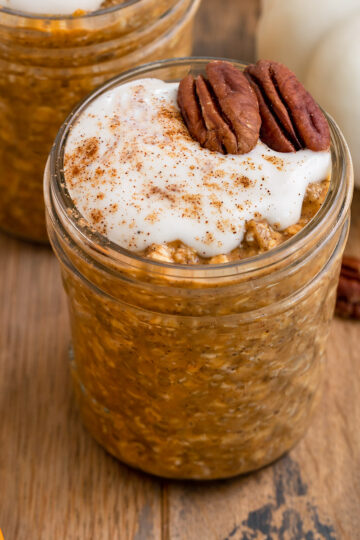 glass container of pumpkin oats with yogurt and pecans on top.