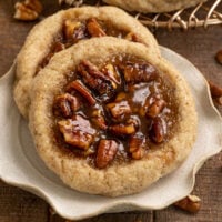 two cookies filled with pecan pie filling on a small plate with tray of cookies behind them.