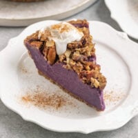 a slice of purple potato pie with streusel, coconut whipped cream, and cinnamon on top.