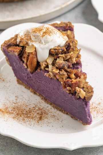 a slice of purple potato pie with streusel, coconut whipped cream, and cinnamon on top.