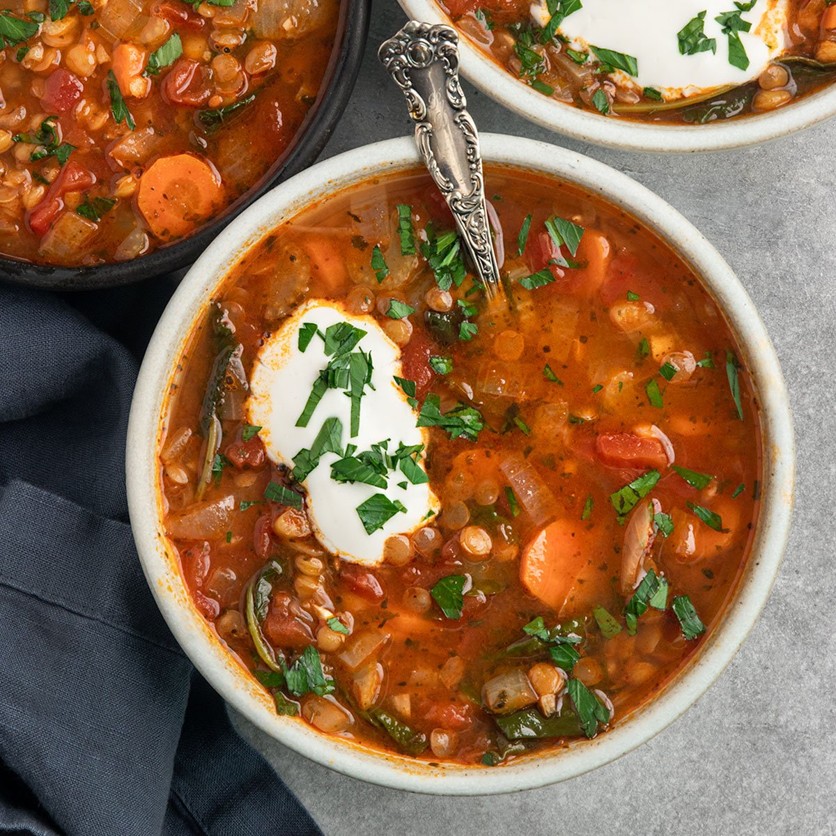 three bowls of vegetable lentil soup with sour cream and fresh parsley on top