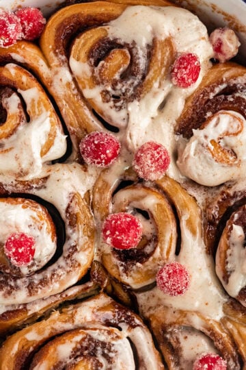 pan filled with gingerbread cinnamon rolls topped with cream cheese frosting and sugared cranberries.