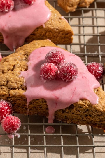 triangular gingerbread scones on a baking tray topped with pink cranberry icing and sugared cranberries.