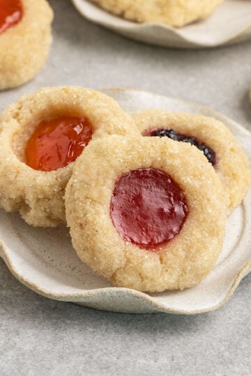 three jam filled cookies on a plate surrounded by more plates of cookies.