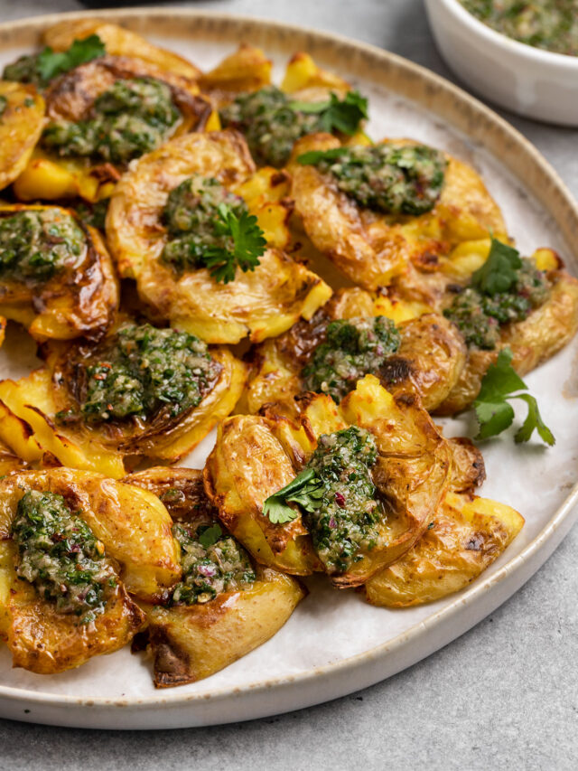 plate of crispy smashed potatoes topped with chimichurri sauce and fresh cilantro.