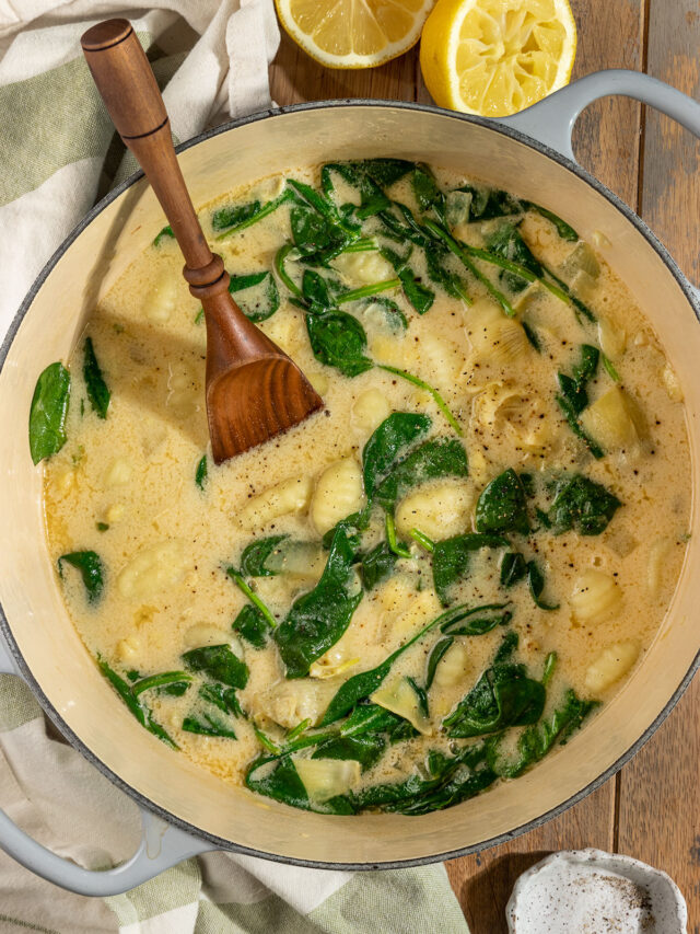 large pot of soup with gnocchi, artichokes, spinach, and a wooden spoon.