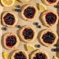 tray of baked lemon cookies filled with blueberry pie filling surrounded by lemon slices and fresh blueberries.