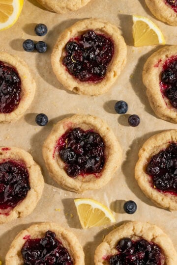 tray of baked lemon cookies filled with blueberry pie filling surrounded by lemon slices and fresh blueberries.