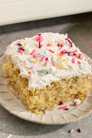 slice of cake topped with buttercream frosting and sprinkles on a small plate.