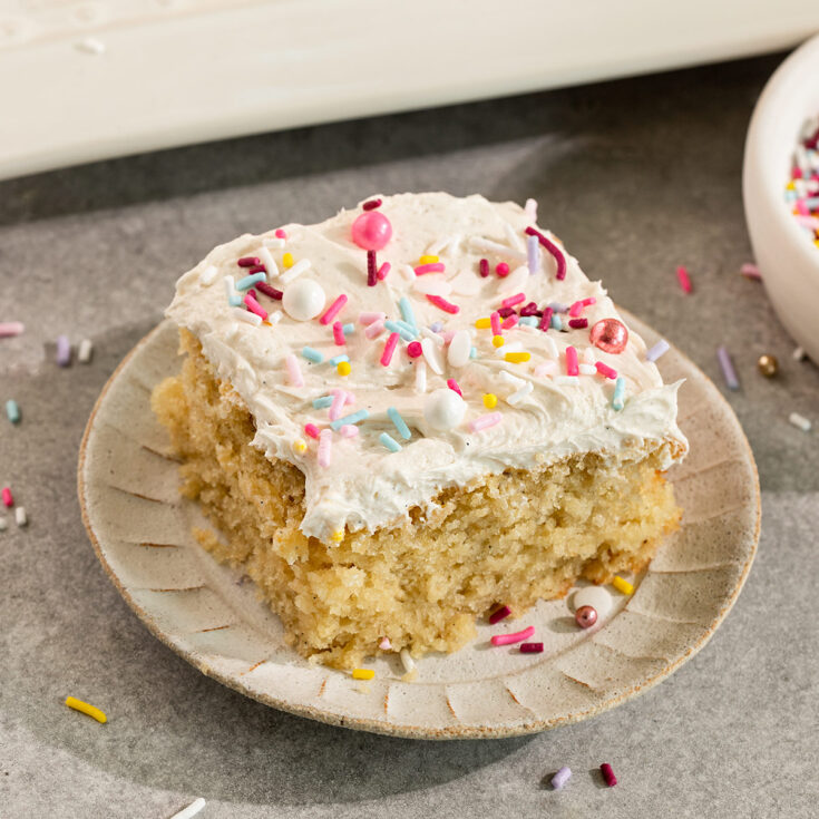 slice of cake topped with buttercream frosting and sprinkles on a small plate.