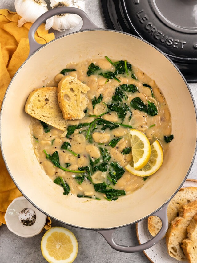 large dutch oven full of creamy butter beans with lemon garlic spinach and slices of toast.