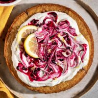 round cake topped with swirls of whipped cream, blueberry jam, lemon slices, and lemon zest.