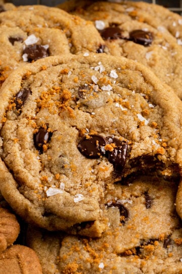 pile of cookie butter chocolate chip cookies with top cookie missing a bite.