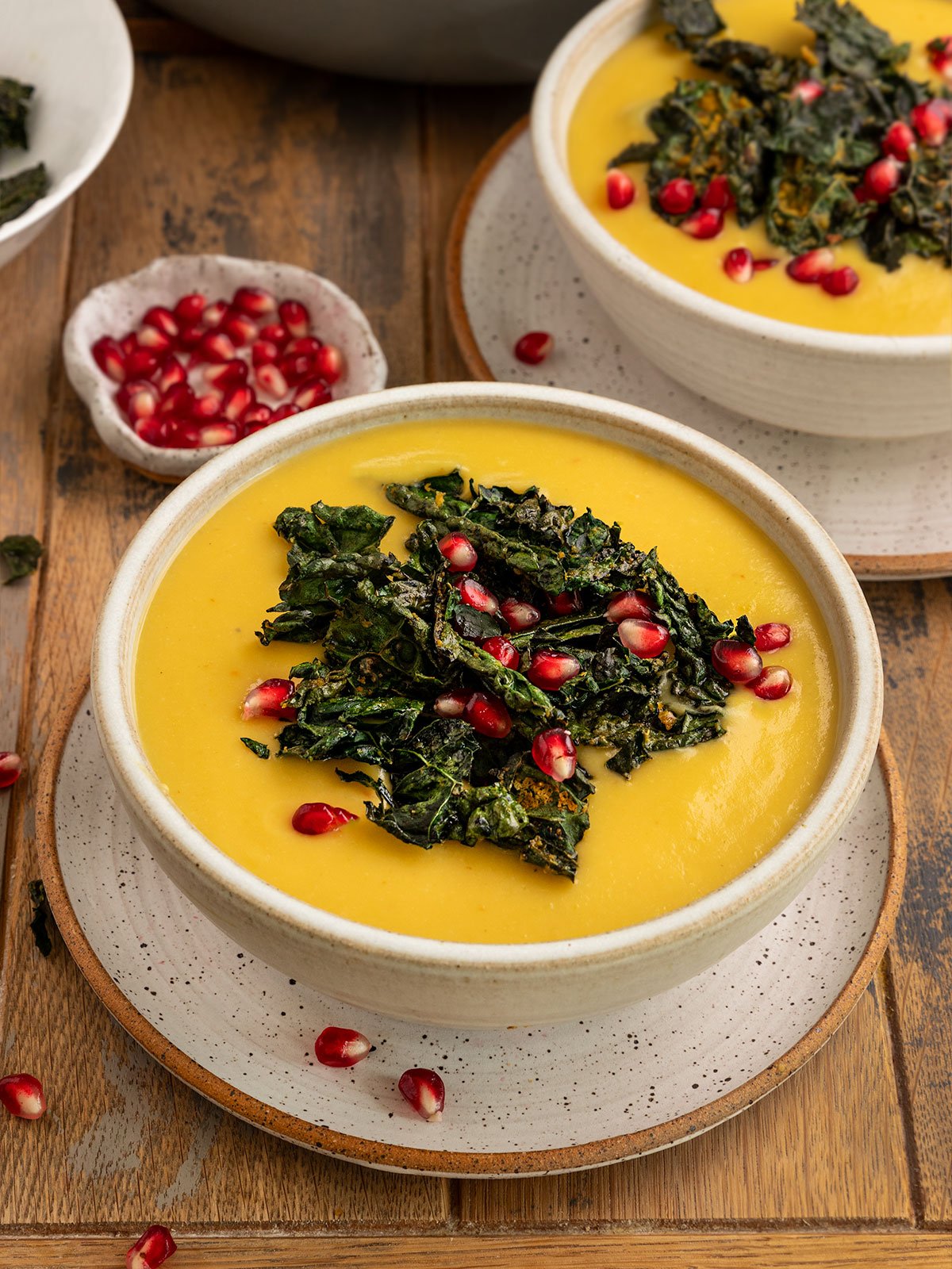 bowls of sweet dumpling squash soup topped with kale chips and pomegranate seeds.
