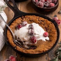 mini cast iron skillets filled with gingerbread chocolate chip cookies, vanilla ice cream, and sugared cranberries with a spoon.