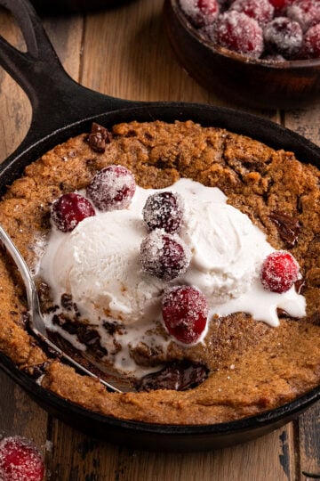 mini cast iron skillets filled with gingerbread chocolate chip cookies, vanilla ice cream, and sugared cranberries with a spoon.