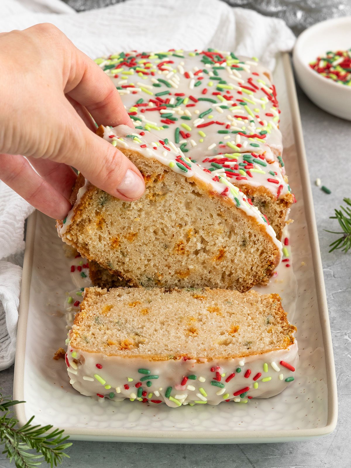 hand lifting a slice of sprinkle bread topped with icing and green and red sprinkles.