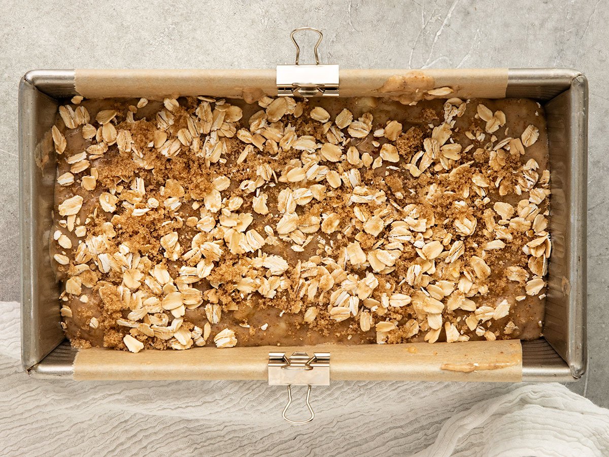 loaf pan filled with banana bread batter topped with rolled oats and brown sugar.