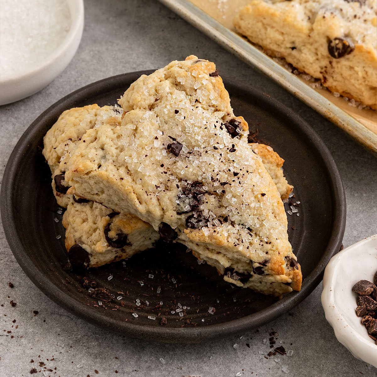 two scones on a plate filled with chocolate chips and topped with coarse sugar.