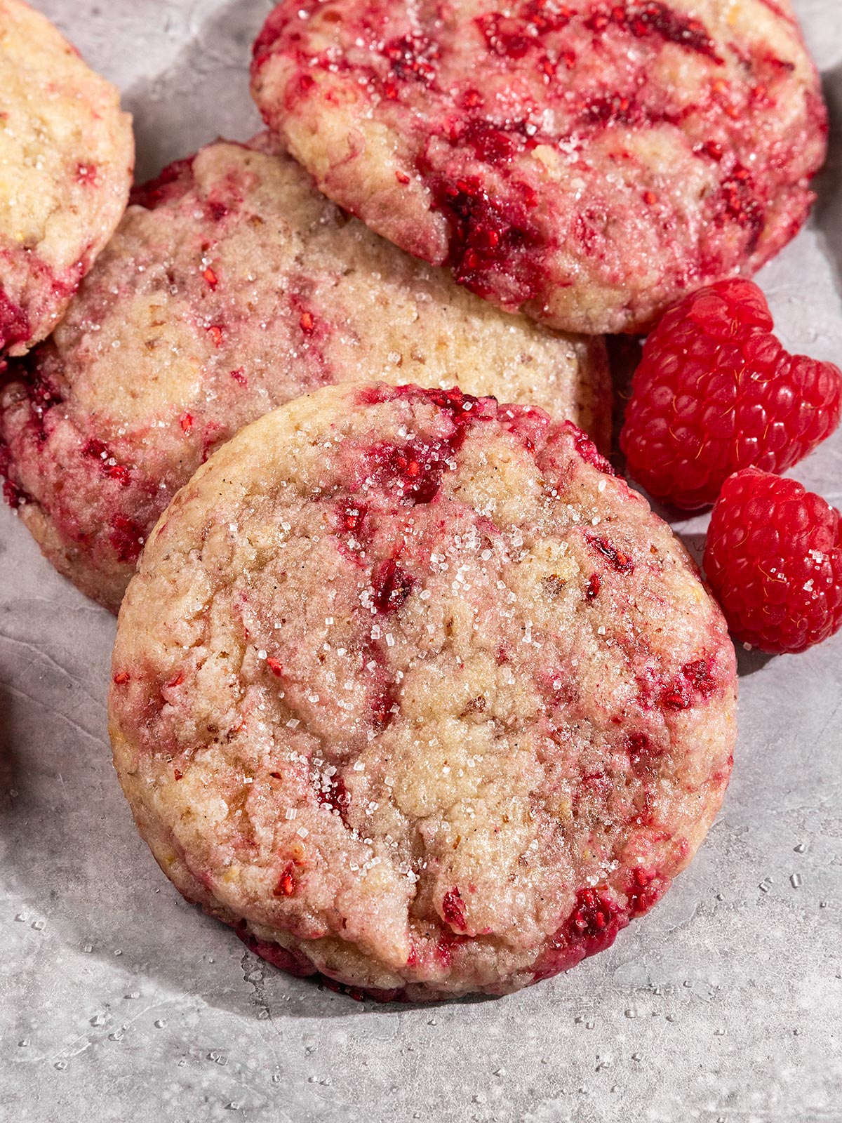 raspberry sugar swirl cookies topped with sparkly sugar and next to fresh raspberries.