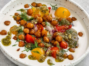 bowls of yogurt topped with crispy chickpeas, tomatoes, cucumber, red onion, dill, and drizzle of pesto.