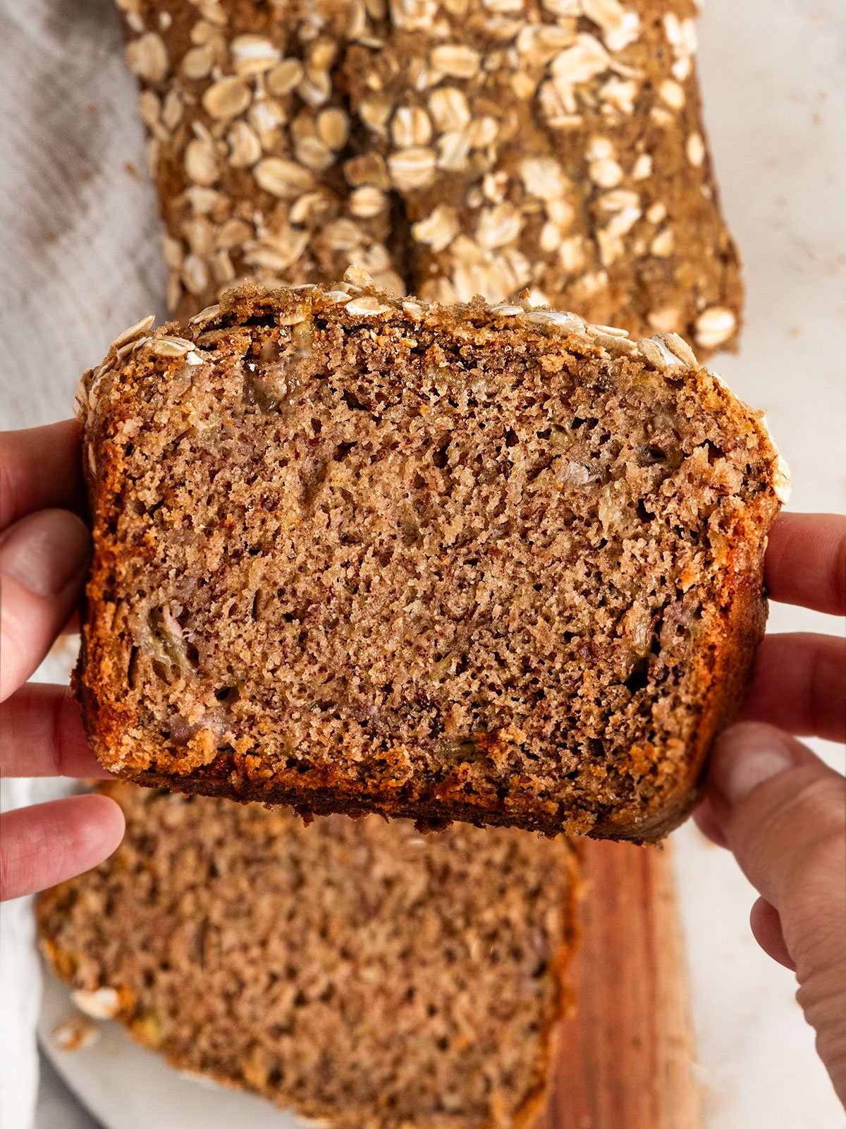 hand holding up slice of banana bread over loaf of bread.